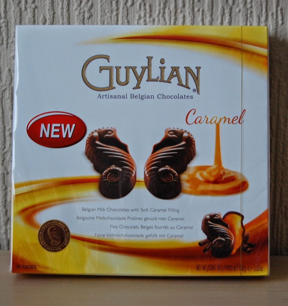 A box of Guylian Caramel Artisanal Belgian Chocolates, perfect for Valentine’s Day gift ideas, features chocolate sea shells with caramel filling on the front, a caramel swirl, the word "NEW," and product details in multiple languages.