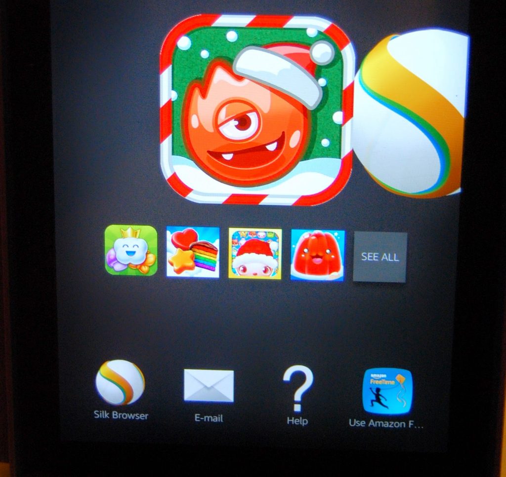 A Kindle Fire HD 6 tablet screen displays app icons, including a monster with a Santa hat, a colourful ball, and icons for Silk Browser, E-mail, Help, and Amazon FreeTime Kids against a black background. Perfect for your next Tablet Review.