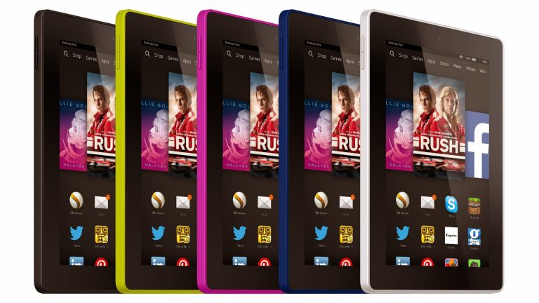 Five Amazon Kindle Fire tablets are shown standing upright in a row, each with a different coloured edge: yellow, green, pink, blue, and white. Their screens display various app icons and media content for this Tablet Review.