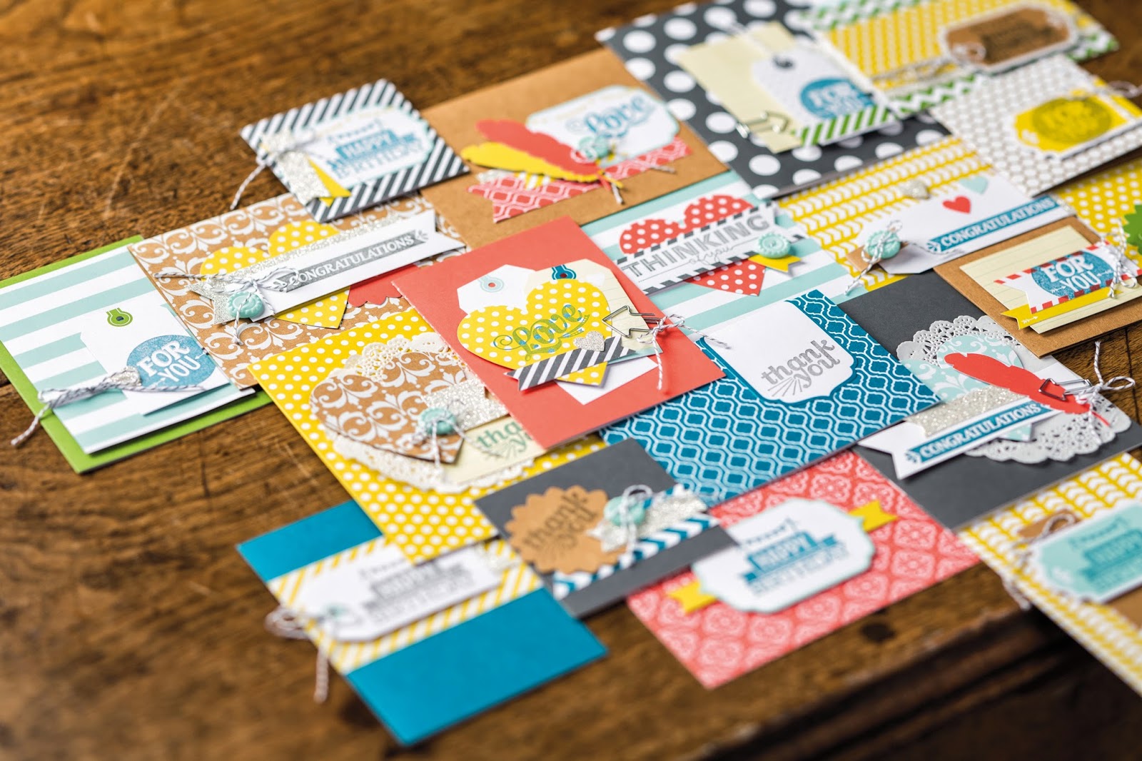 A variety of colourful handmade greeting cards with different patterns, tags, and embellishments are spread out on a wooden surface—plus, you could Win an Everyday Occasions Card Making Kit to create your own heartfelt “thank you” or “congratulations” cards.