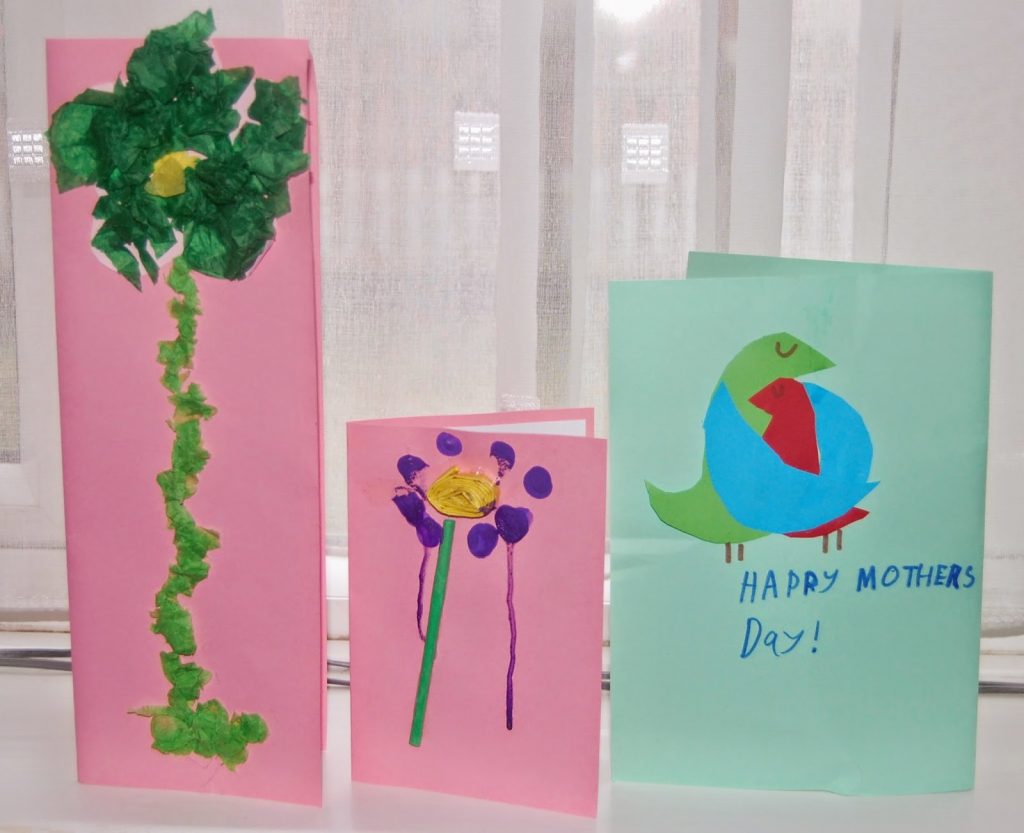 Three handmade Mother’s Day cards stand on a windowsill for Silent Sunday: one has a tall green flower made from tissue paper, another shows a painted flower, and the third features a colourful bird with “Happy Mother’s Day!” written on it.