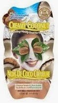 A sachet of Montagne Jeunesse Creamy Coconut face mask, perfect for a Pamper Hamper, featuring a smiling woman with a white mask, leaves over her eyes, and coconut halves in the background. Text is in English and French.