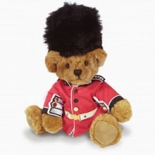 A classic teddy bear dressed in a red British guard uniform and a tall, black bearskin hat sits against a plain white background.