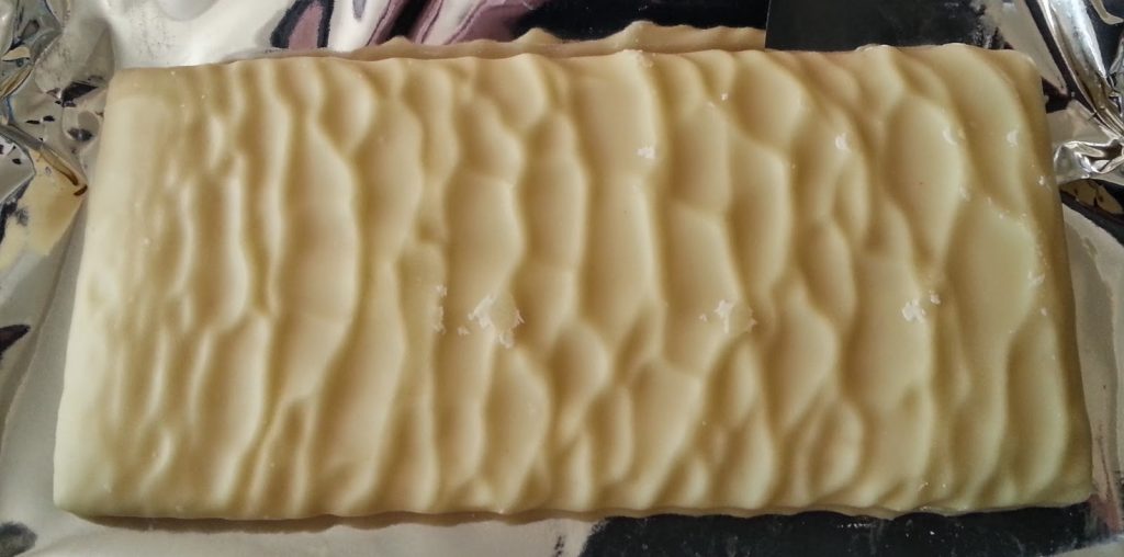 A close-up of a rectangular white chocolate bar with a wavy, textured surface, partially unwrapped from silver foil—one of those tasty little numbers that’s hard to resist.
