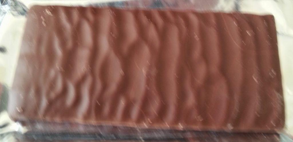 A close-up of a rectangular chocolate-covered wafer with a wavy, textured surface, resting on a metallic wrapper—one of those tasty little numbers perfect for satisfying your sweet tooth.