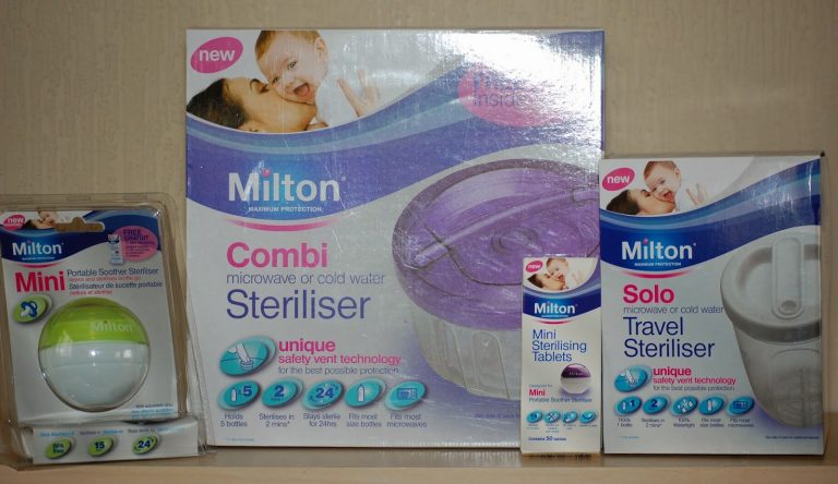 Milton steriliser products on a shelf, including a mini soother steriliser, combi steriliser, sterilising tablets, and a solo travel steriliser—each in branded packaging featuring images of a baby and carer.