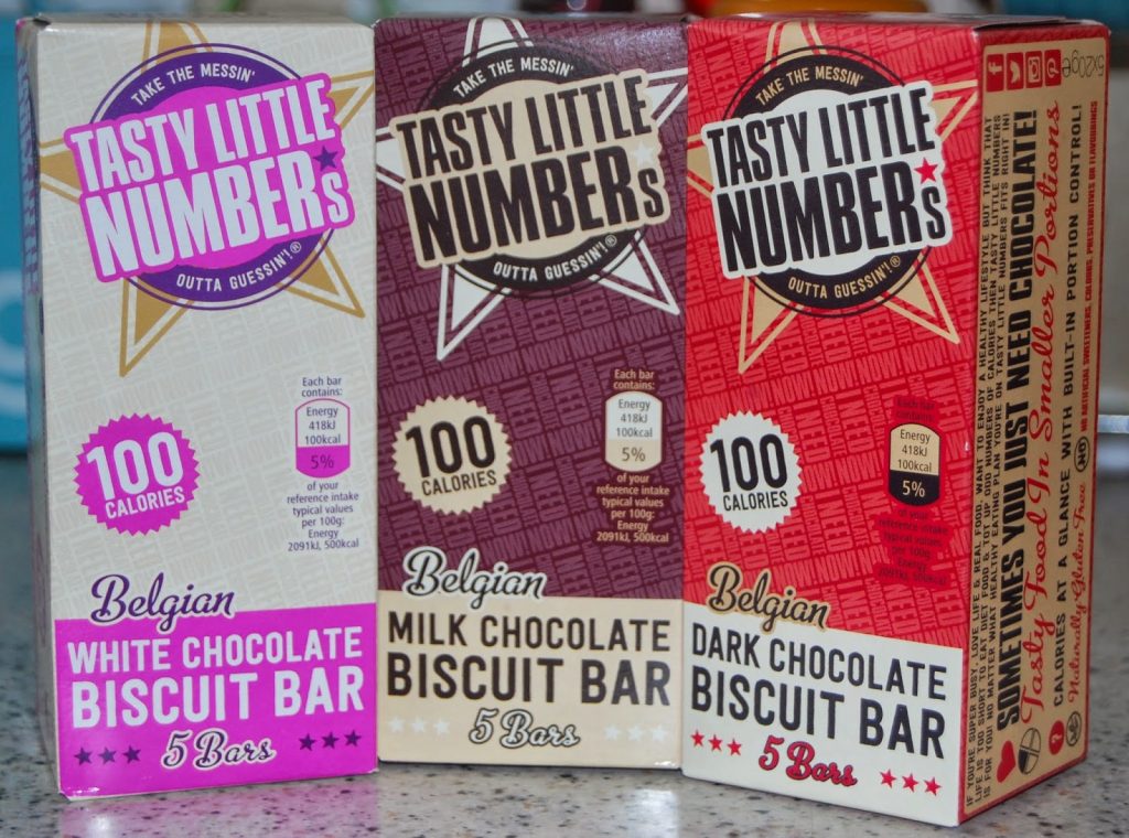 Three boxes of tasty little numbers Belgian biscuit bars—white, milk, and dark chocolate varieties. Each box holds 5 bars at 100 calories each, lined up side by side on the counter.
