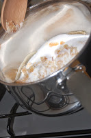 A stainless steel saucepan on a hob contains caster sugar, brown sugar, and what appears to be a vanilla pod for the Heston Pear Tarte Tatin Challenge, with a wooden spoon resting on the side.