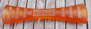 An orange, bone-shaped rubber dog toy with ridges and the word "Rogz" embossed in the centre, lying on a wooden surface, perfect for those seeking a durable alternative like the Bionic Urban Stick.