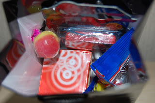 An overhead view of a bag filled with colourful packaged snacks and sweets, perfect for James' birthday celebration. The treats include a red and yellow round sweet and several red and blue rectangular wrappers—ideal for turning 6!.
