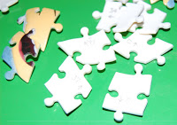 Several white and partially coloured Ravensburger jigsaw puzzle pieces are scattered on a bright green surface.