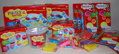 A variety of Plasticine Softeez modelling clay sets in colourful packaging, including boxes, tubs, and individually wrapped clay blocks, are arranged together with two sticker sheets in the background—perfect for your next Twitter Party.