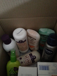 A cardboard box filled with various personal care products, including bottles of lotion, shampoo, and deodorant from brands like Hawaiian Tropic, Aussie, Nivea, and V05—just the kind of selection you’d find at Chemist Direct.