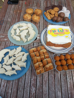 A wooden table with various snacks, including dolphin-shaped white biscuits, muffins, round treats, and a cake with white icing and a "Plasticine Softeez" label—perfect for a Twitter Party spread.