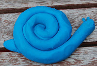 A blue snail made of Plasticine Softeez modelling clay sits on a weathered wooden surface, ready to join the fun at your next Twitter Party.