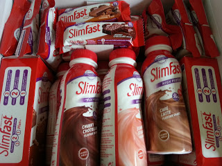 Assorted SlimFast products, including meal replacement shakes and bars in various flavours, are arranged closely together in a box. The packaging features red, white, and brown colours—perfect for your SlimFast challenge or weight loss journey.