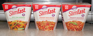 Three SlimFast meal boxes—Spicy Thai Noodles, Chicken Tikka Masala, and Spaghetti Bolognese—sit on a worktop. Each features purple and white packaging with meal images, perfect for the SlimFastWorksForMe Challenge and supporting your weight loss goals.