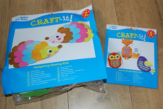 Two colourful sewing kits are shown on a wooden surface, perfect for autumn crafts. The larger kit features a hedgehog design, while the smaller kit displays owl and bird motifs. Both packages have bright blue labels titled "CRAFT-it!".