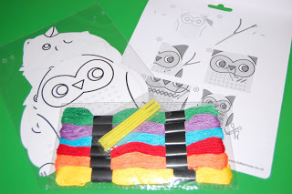 A craft kit for autumn crafts with coloured threads, yellow sticks, and two owl-themed templates for string art on a green surface. The templates feature owl faces with numbered sections for threading.