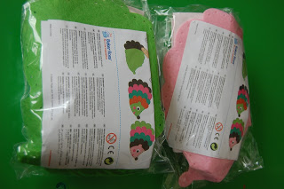 Two sealed plastic bags contain colourful autumn crafts kits with hedgehog designs (one green, one pink), each including an instruction sheet displaying text and images on the front.
