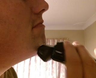 A person shaving their chin with a Braun Series 5 electric razor in a softly lit room, light-coloured curtains in the background.