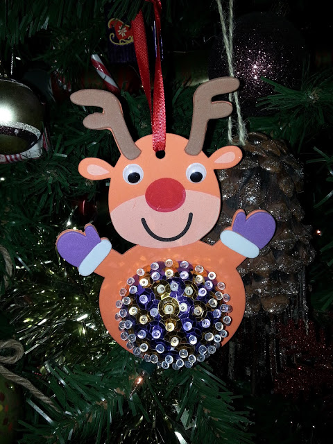 Flashback Friday: A handmade reindeer ornament with googly eyes, a red nose, purple mittens, and a beaded belly hangs on the Christmas tree, sparkling with colourful sequins and beads.
