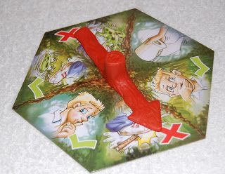 A hexagonal game spinner, inspired by Og On The Bog, features cartoon faces with various expressions and a large red arrow pointing to a worried blond boy. The background shows greenery and red X marks.