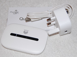 A white Huawei E5573 4G Mobile Wi-Fi hotspot device, a three-pin UK power adaptor, a USB charging cable, and a quick start guide are neatly arranged on a light surface.