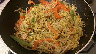 A wok filled with stir-fried noodles, bean sprouts, sliced red peppers, green beans, and tender meat—perfect for a cosy Date Night or sharing at the Amoy Supper Club. The ingredients appear freshly cooked and well-mixed.