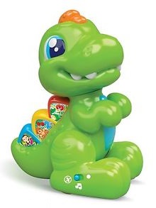 A green, cartoon-style dinosaur toy with big blue eyes, colourful buttons on its back, and a small musical note on its foot. This friendly, playful toy makes a delightful choice for new parent gifts.