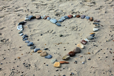 A heart shape made from variously coloured stones is arranged on a sandy beach, with small scattered pebbles around it, creating a beautiful scene perfect for celebrating a 10 year anniversary.