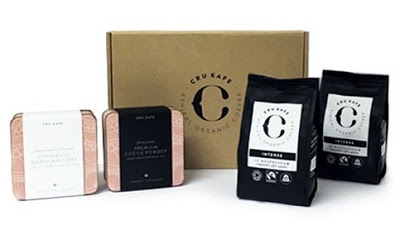 A set of CRU KAFE organic coffee products, including two tins, two black coffee bags, and a brown box with the brand’s logo—perfect for crafting festive beverages or adding a rich touch to your holiday cocktails.