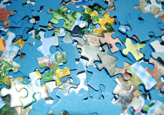 A close-up view of several scattered jigsaw puzzle pieces, showing both the blue backs and some colourful front sides with various patterns—perfect for lovers of puzzle fun.