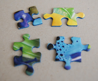 Four colourful jigsaw puzzle pieces with blue, green, and yellow patterns are placed on a light beige surface. Perfect for some Puzzle Fun, the pieces are not connected and arranged in two rows.