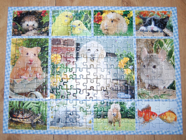 A completed jigsaw puzzle featuring various animal photos—hedgehog, birds, guinea pig, kitten, hamster, dog, chinchilla, tortoise, rabbit, and two goldfish—all bordered by a blue and white chequered frame for extra puzzle fun.