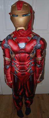 A child stands indoors in a red and gold Iron Man costume, complete with a mask and padded suit, ready for their own hero adventure, in front of a white door and wooden floor—perfect for an Iron Man costume review.