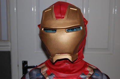 A person wearing an Iron Man costume and mask stands indoors in front of a white door. This Iron Man costume features gold, red, and silver colours, with only the mask and upper body visible—perfect for any costume review.