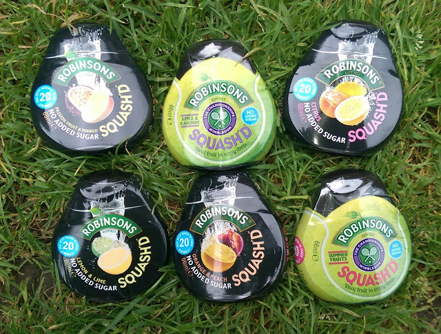 Six bottles of Robinsons Squash'd concentrated drink in various flavours are arranged on green grass. Each bottle displays its flavour and label, inviting you to Enjoy More Water with apple & blackcurrant, lemon & lime, and passion fruit & mango.