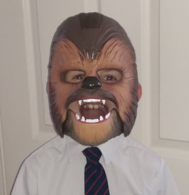 A person wearing a Chewbacca mask, a white shirt, and a dark striped tie stands in front of a white panelled door—perfect for your next Harleys Glitter Jelly Review.