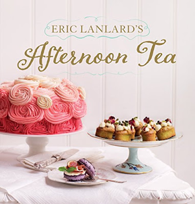 A pink ombré rosette cake, small decorated pastries on a cake stand, and purple macarons are displayed on a white tablecloth. The text "Eric Lanlard's Afternoon Tea" is shown above—perfect for pairing with your August book recommendations.