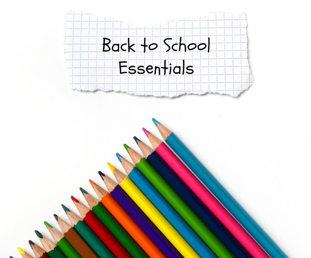 A row of colourful pencils arranged diagonally with a torn piece of graph paper above them that reads “Back to School Essentials” in a handwritten style, highlighting must-have back to school essentials on a plain white background.