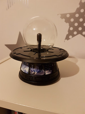 A Star Wars-themed Energy Ball with a black base displaying film images sits on a white surface. A grey wall with star patterns is in the background, making it look like Force Lightning from the films.