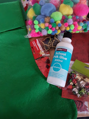 Craft supplies including green felt, a bottle of school PVA glue, colourful pom-poms, assorted jingle bells, and festive decorations are laid out on a surface—perfect for Make It Don't Buy It Christmas gifts or creative DIY projects.