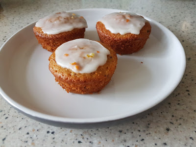 Three small cupcakes made with a Zesty Carrot Cake recipe, topped with white icing, are arranged on a white plate, set on a speckled worktop.