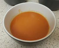 A white bowl filled with smooth, orange soup sits on a speckled worktop, perfect for festive recipes and holiday cooking.