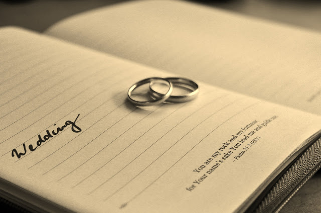 Two wedding rings rest on an open notebook. The word “Wedding” is written on one page, and a Bible verse graces the other. The sepia tones evoke a warm, nostalgic mood perfect for remembering your special wedding day.
