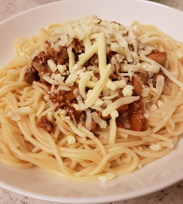 A plate of cooked spaghetti topped with a rich Dolmio tomato-based meat sauce, diced vegetables, and a generous sprinkle of grated cheese.