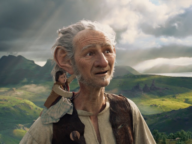 A giant with grey hair and large ears stands outdoors under a cloudy sky, while a small girl sits on his shoulder, holding onto his ear. It's the perfect Half Term adventure to watch together—now streaming on Amazon Prime.