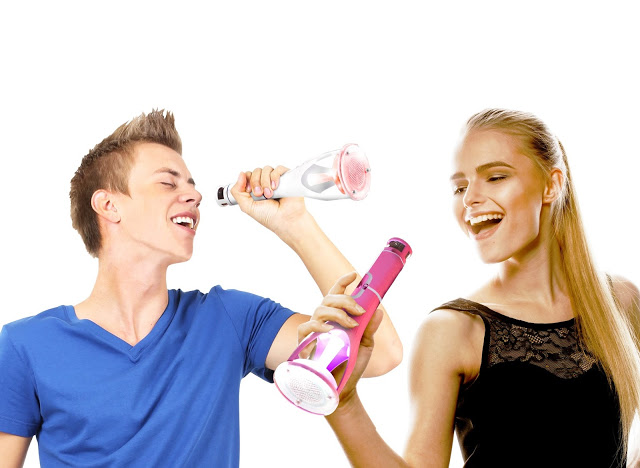 A young man and woman smiling and pretending to sing into cordless vacuum cleaners like microphones, as if they're using a Rocket Singing Machine, against a white background.