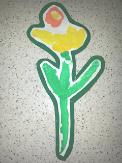 A child’s painting of a yellow flower with green stem and leaves, outlined in green, on a speckled light background. Are You Guilty of Throwing Away Your Child's Artwork? This charming piece showcases an orange centre.